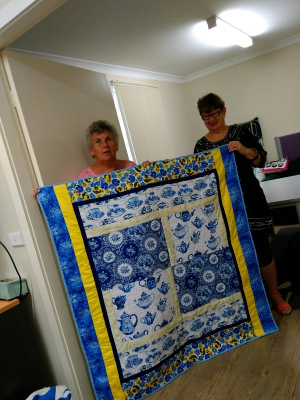 Dearnne Callaghan and Karen Willis holding up the quilt that was donated to Cedar Cafe.